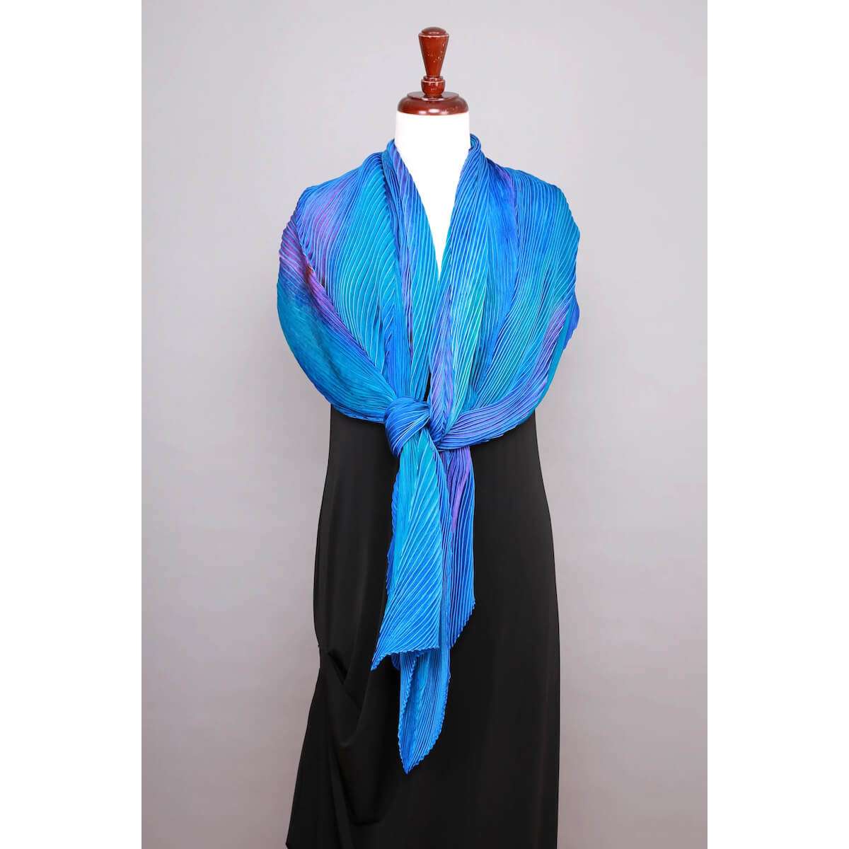 An open and flowing style of draping of the Cathayana silk shibori shawl on a dress form, displaying the large fabric size and fluid, light-catching movement of the pleated silk.